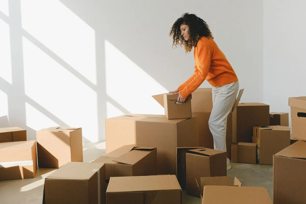 Young woman with curly hair packing cardboard boxes while preparing to move into a new apartment.