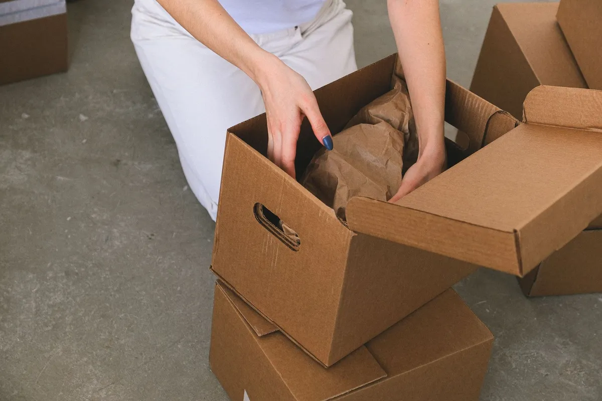 A woman packs wrapped items into a box, illustrating the moving process discussed in the article.