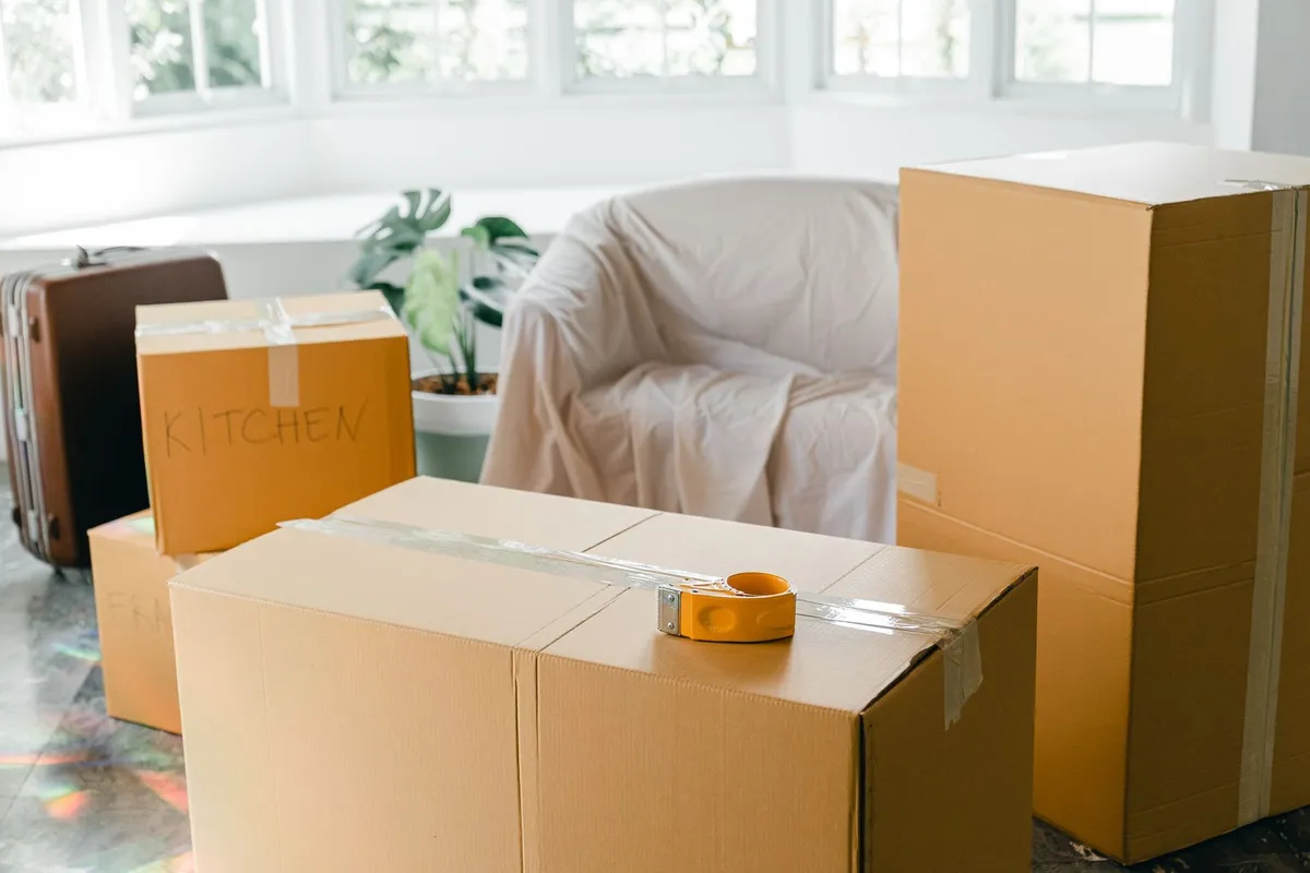 Cardboard boxes and a suitcase filled with belongings in a bright room before moving to a new apartment.